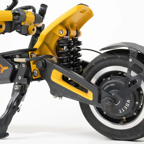 Izdelek na sliki je električni skiro, model Vsett 11 Super. Vidna je zadnja stran skiroja, kjer so prikazani amortizerji in zadnje kolo. Barvna kombinacija je črna in rumena, kar daje skiroju dinamičen videz. Amortizerji so zasnovani za boljšo udobnost pri vožnji, kar je pomembno za uporabo na različnih terenih.