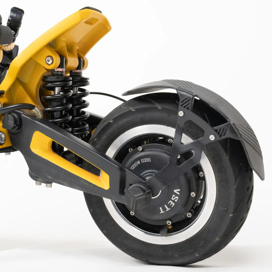 Na sliki je električni skiro znamke Vsett, model 11 Super. Prikazan je zadnji del skiroja, kjer so vidni vzmeti za blaženje udarcev ter široko zadnje kolo z močnim motorjem. Kolo ima robusten profil, kar omogoča boljšo stabilnost in oprijem na različnih površinah. Skupna zasnova kaže na visoko kakovost in zmogljivost, primerna za mestno vožnjo.