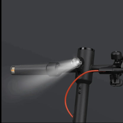 Na sliki je električni skiro znamke Xiaomi, model Elite. Vidna je ročica skiroja s svetilko, ki je nameščena na krmilu, ter rdeč kabel, ki se verjetno povezuje z električnim sistemom. Ozadje je temno, kar poudarja detajle skiroja in svetlobe.