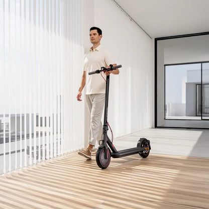 Oseba se sprehaja z električnim skirojem Xiaomi 4 Eu v moderni, s soncem obsijani notranjosti.