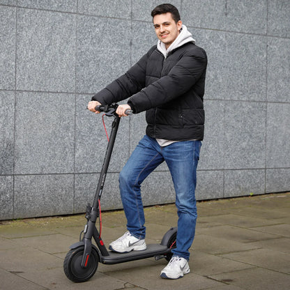 Oseba v črni jakni vozi električni skiro Xiaomi 4 Eu ob sivi steni.
