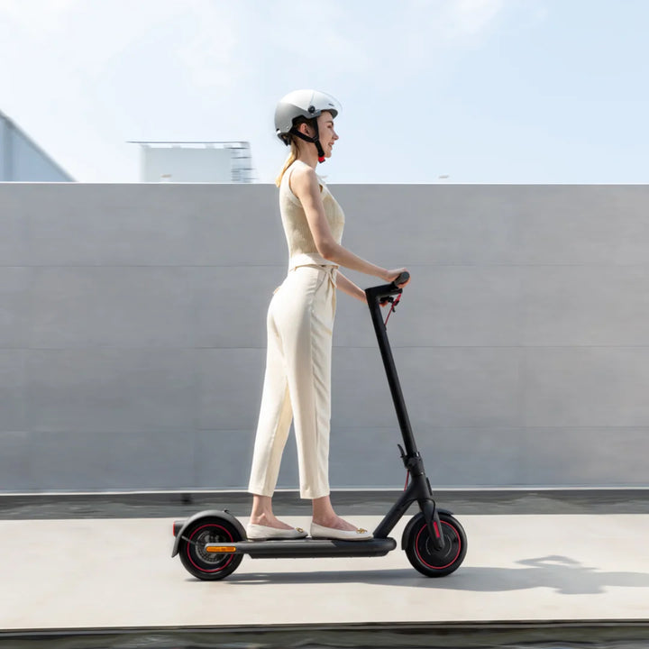 Oseba vozi električni skiro Xiaomi 4 Eu, nosi čelado in je oblečena v priložnostna oblačila.