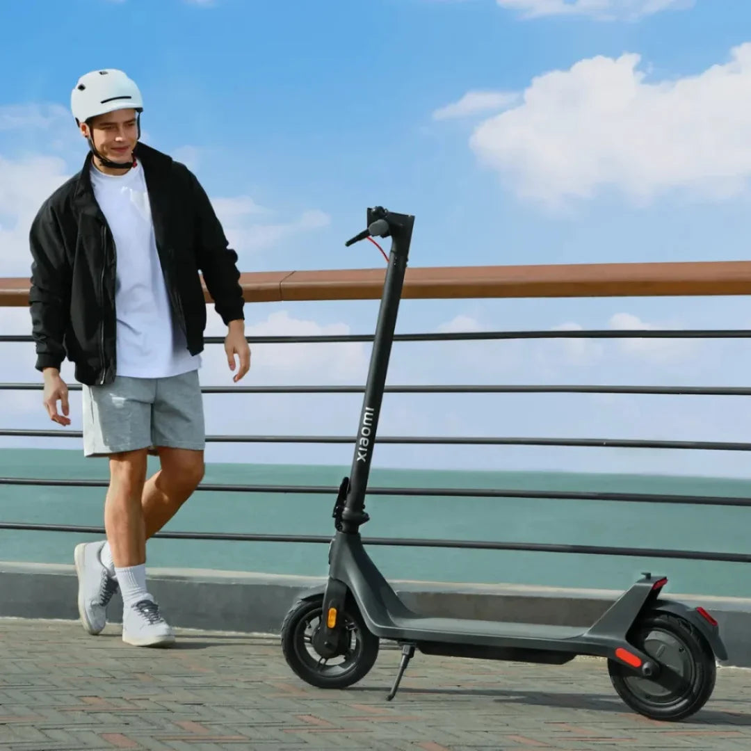 Oseba s čelado stoji ob električnem skiroju Xiaomi 4 Lite 2nd Gen ob morju.