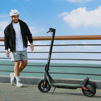 Oseba s čelado stoji ob električnem skiroju Xiaomi 4 Lite 2nd Gen ob morju.