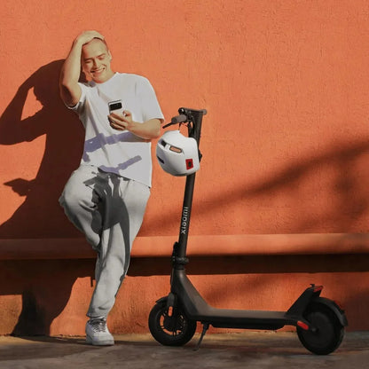 Oseba v neformalnih oblačilih preverja svoj telefon poleg električnega skiroja Xiaomi 4 Lite 2nd Gen.