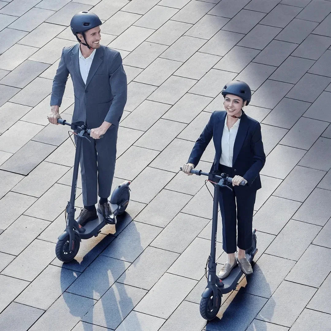 Dve osebi v poslovnih oblačilih se vozita z električnim skirojem Xiaomi 4 Pro 2. generacije na tlakovani površini.