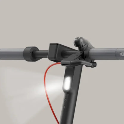 Izdelek na sliki je električni skiro, znamke Xiaomi, model 5 Max GL. Na sliki je prikazan del krmila skiroja, kjer so vidni ročaji, lučka in gumb za zvonec. Skupna zasnova je moderna in funkcionalna, kar omogoča udobno vožnjo.