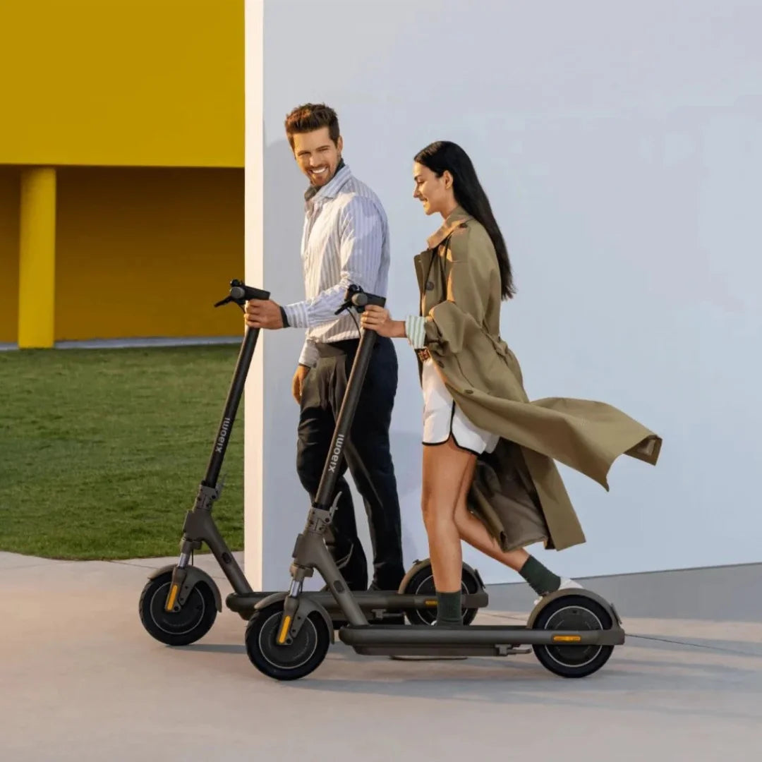 Moški in ženska hodita ob električnem skiroju Xiaomi 5 Max GL v modernem zunanjem okolju.