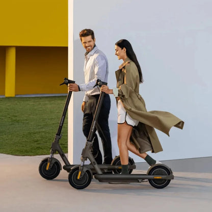 Moški in ženska hodita ob električnem skiroju Xiaomi 5 Max GL v modernem zunanjem okolju.