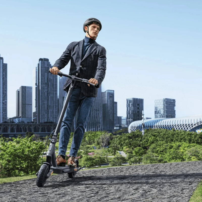 Moški se vozi z električnim skirojem Xiaomi 4 Ultra v mestnem parku z nebotičniki v ozadju.