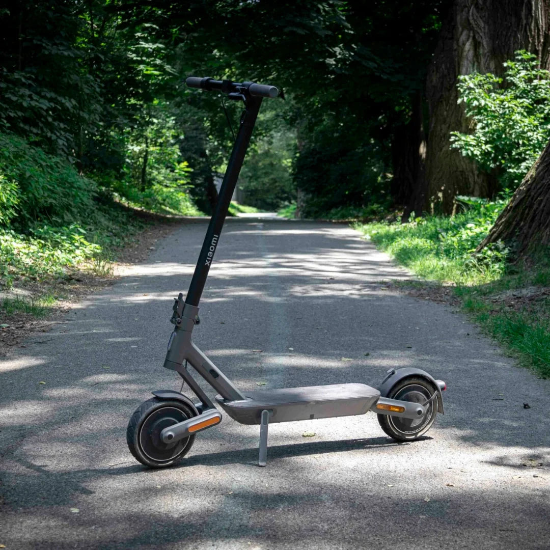 Električni skiro Xiaomi 4 Ultra parkiran na poti, obdani z drevesi.