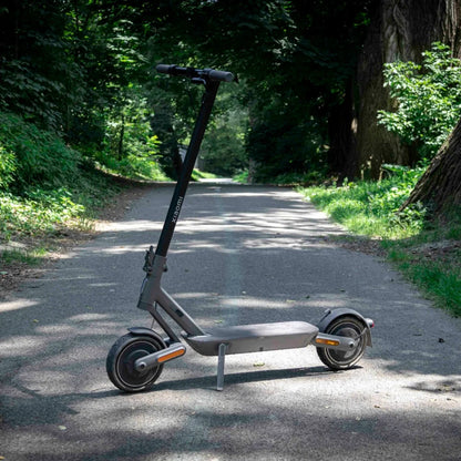 Električni skiro Xiaomi 4 Ultra parkiran na poti, obdani z drevesi.