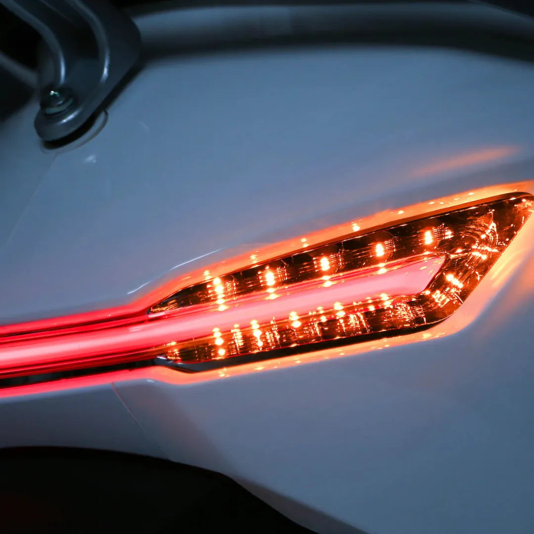 Od blizu posnet repni luči električnega skuterja Yadea C Umi, ki sveti oranžno.