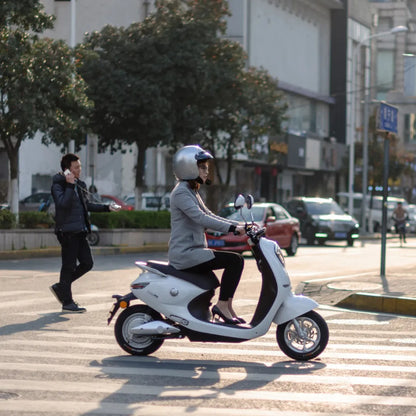 Ženska se vozi z električnim skuterjem Yadea C Umi na prehodu za pešce v mestnem okolju.