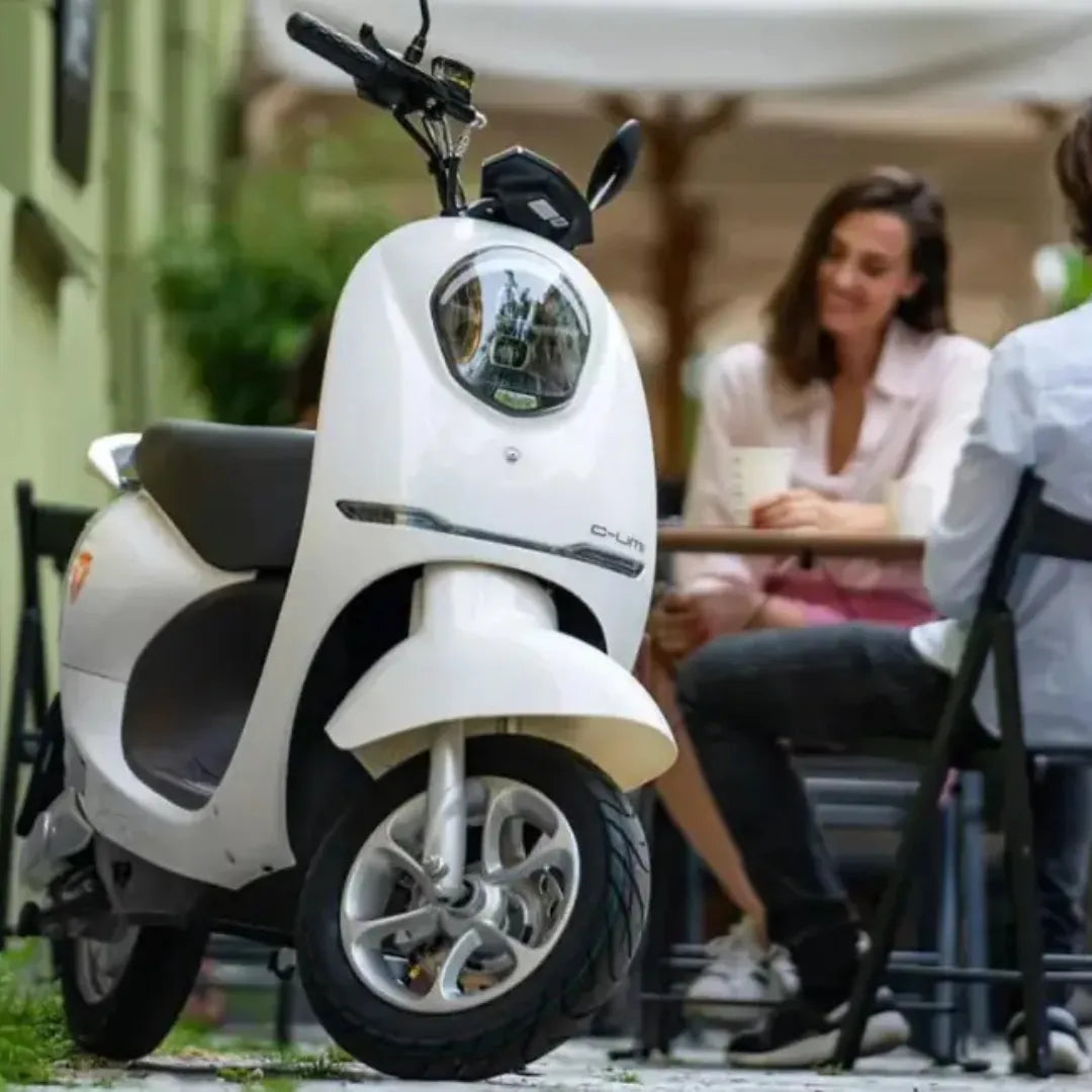 Beli električni skuter Yadea C Umi parkiran blizu ženske za mizo v kavarni.