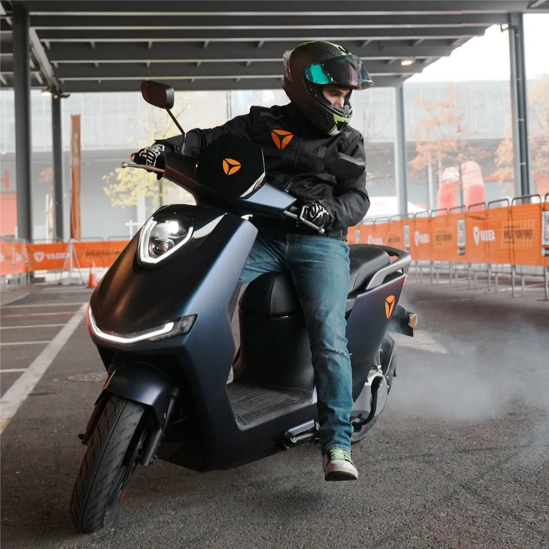 Voznik električnega skuterja Yadea Fierider, s čelado in jakno, v urbanem okolju.