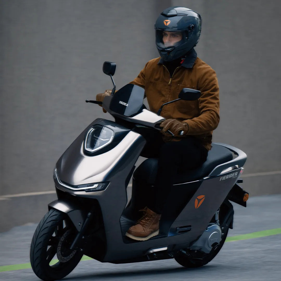 Voznik električnega skuterja Yadea Fierider, ki nosi čelado in rjavo jakno.