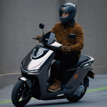 Voznik električnega skuterja Yadea Fierider, ki nosi čelado in rjavo jakno.