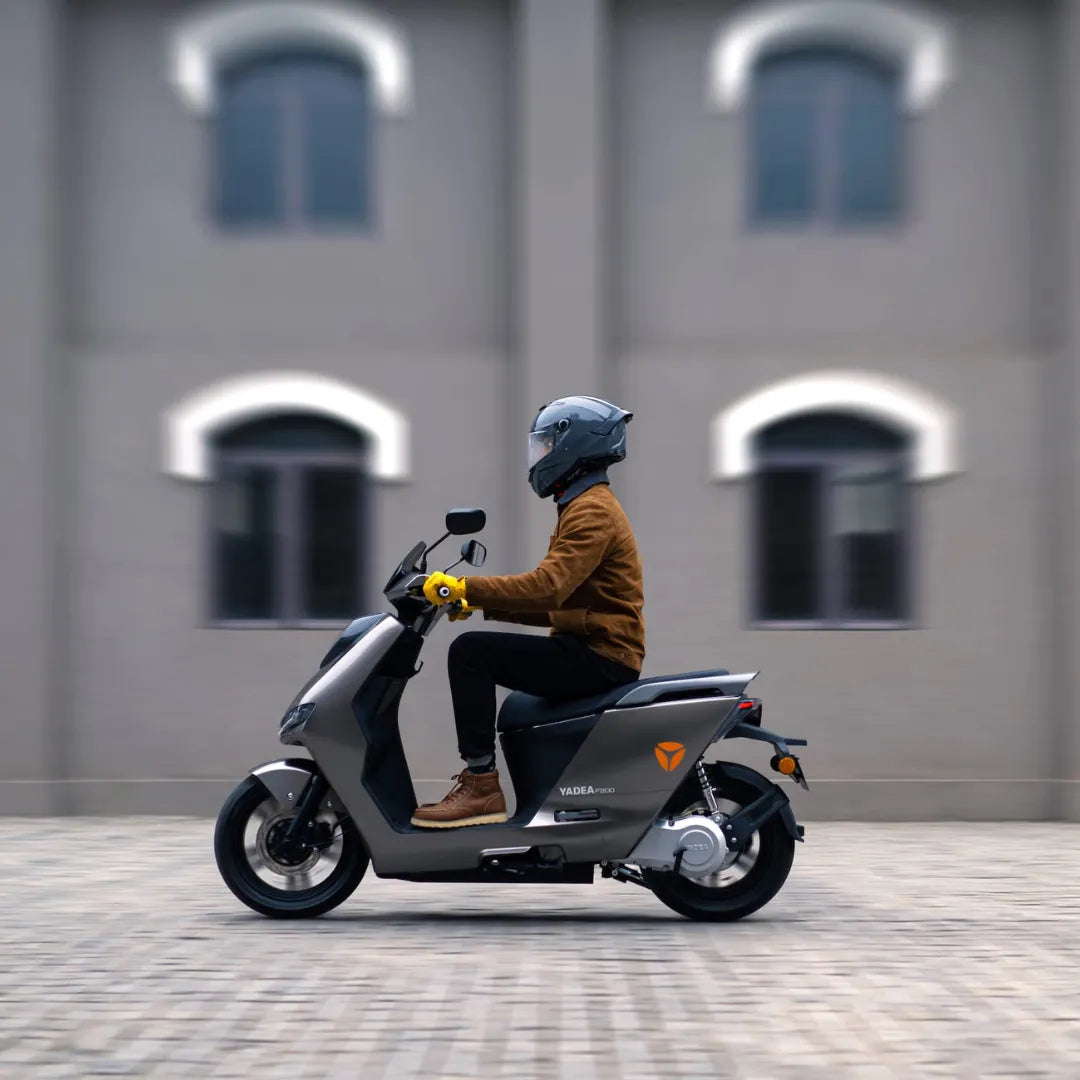 Oseba se vozi z električnim skuterjem Yadea Fierider po mestni ulici.