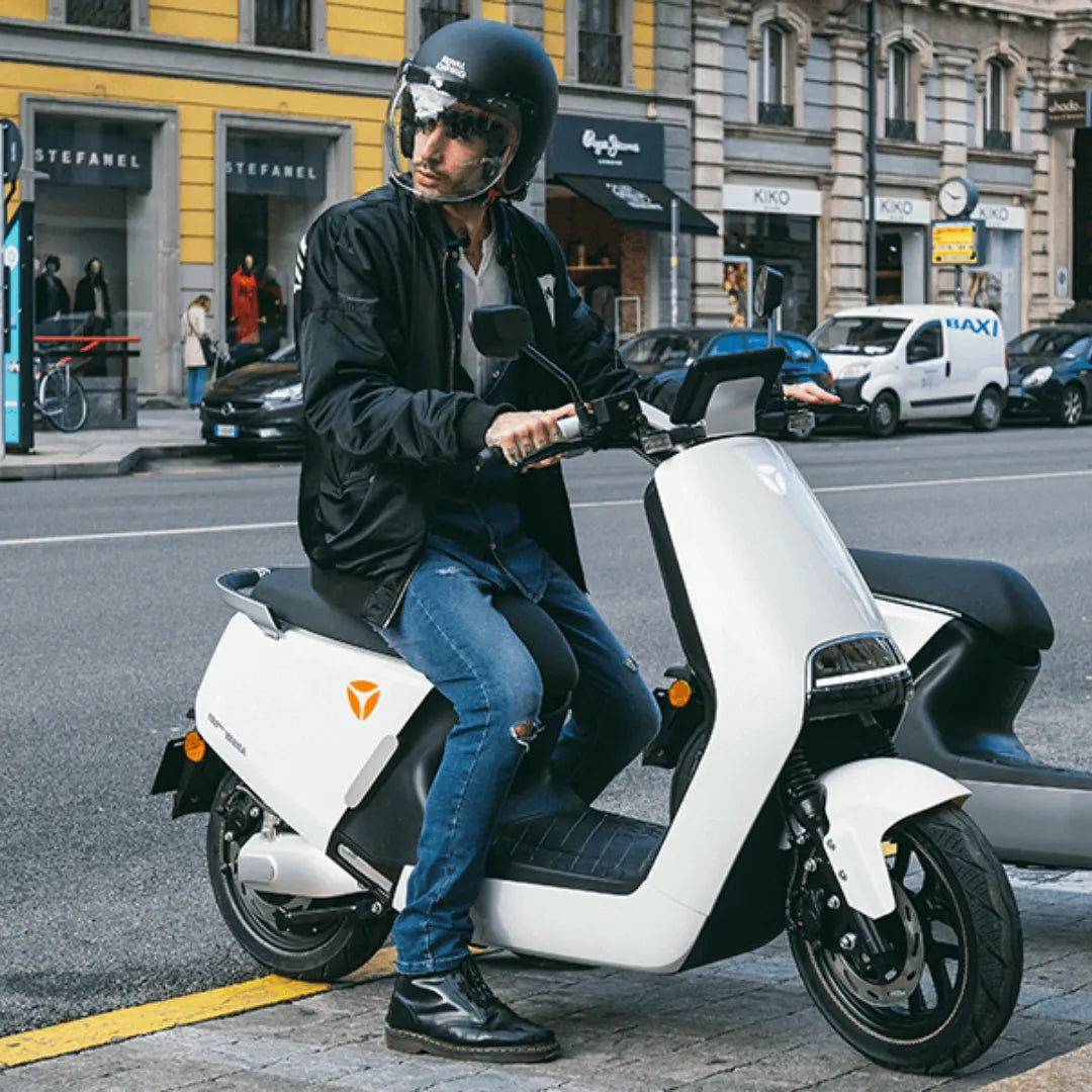 Voznik s čelado sedi na električnem skuterju Yadea G5 na mestni ulici.