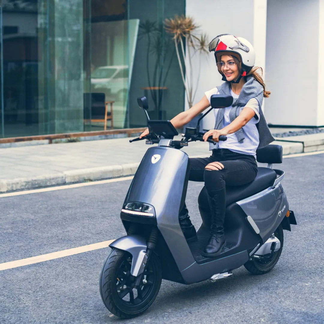Ženska vozi električni skuter Yadea G5, nosi čelado, na mestni ulici.