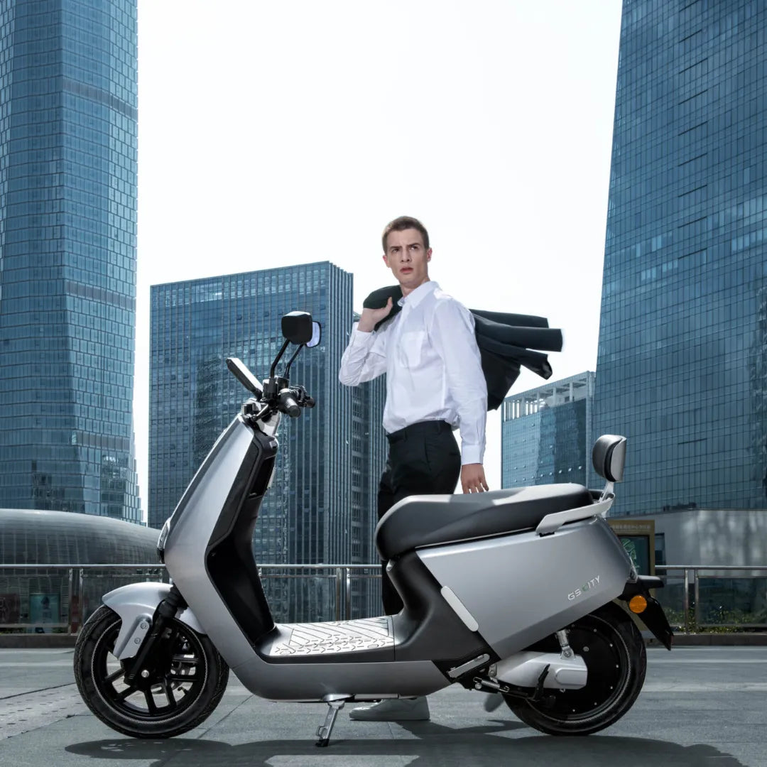 Moški v obleki stoji ob električnem skuterju Yadea G5 v urbanem okolju.