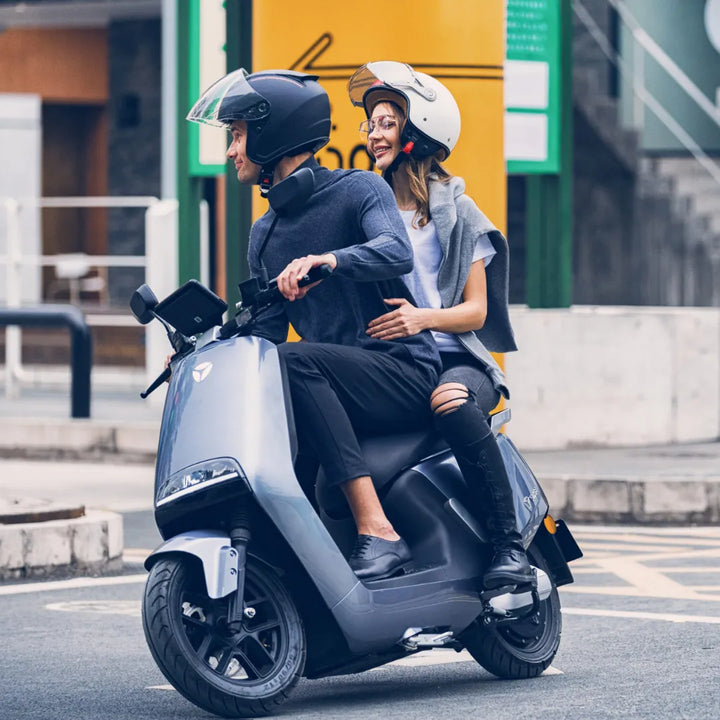 Par se vozi z električnim skuterjem Yadea G5 po mestni ulici, oba nosita čelado.
