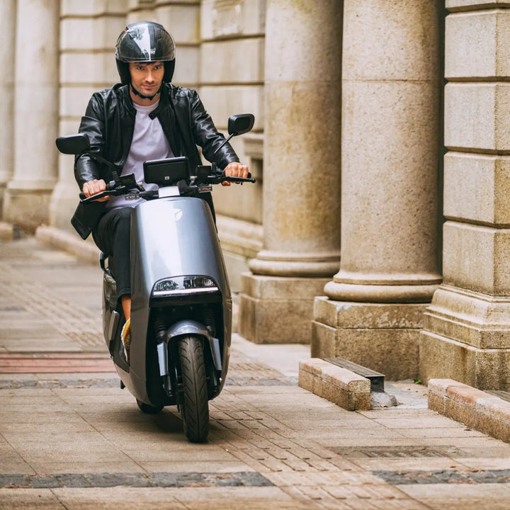 Voznik na električnem skuterju Yadea G5 se vozi po ulici, tlakovani s kamnom.