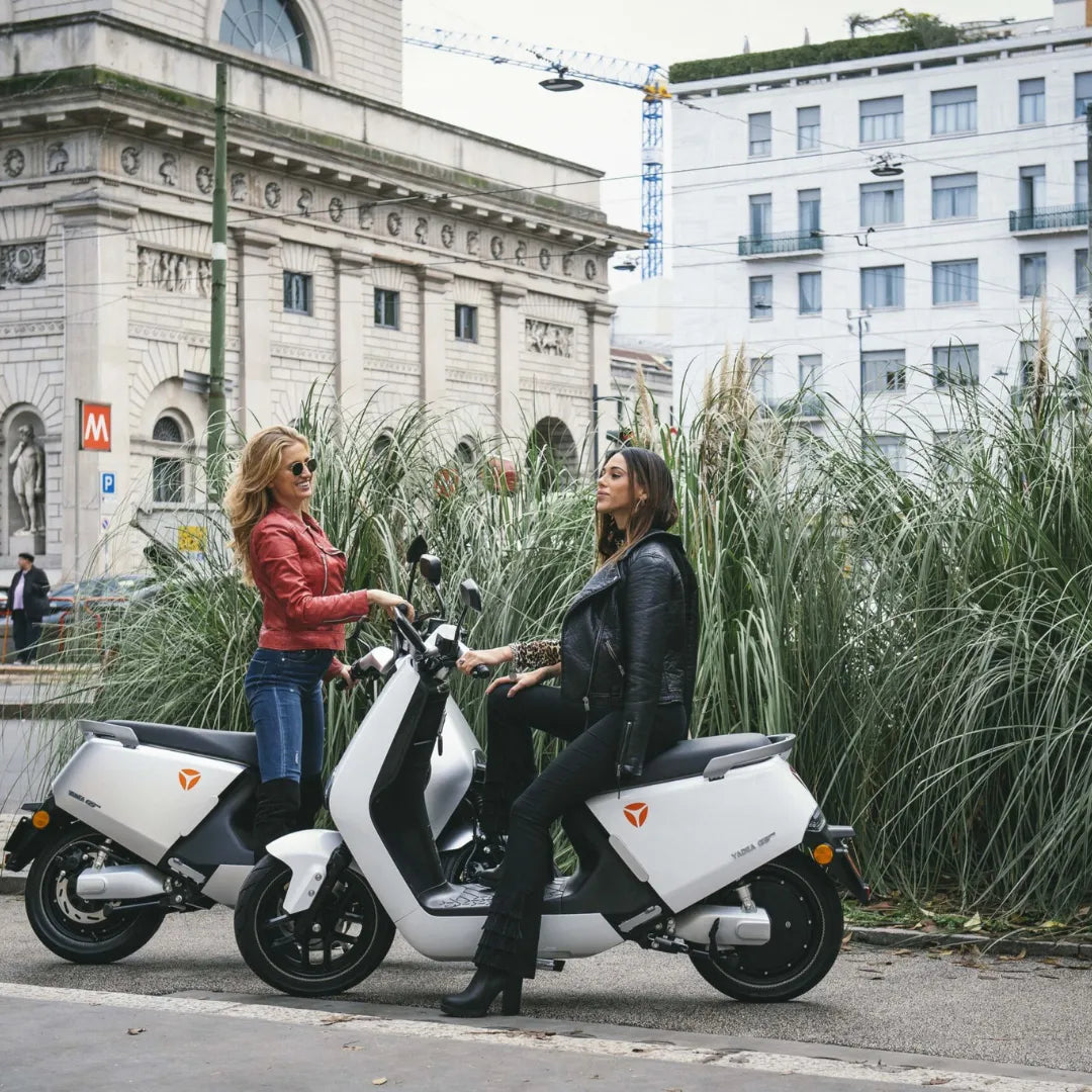 Dve ženski v elegantnih jaknah stojita ob električnem skuterju Yadea G5 v urbanem okolju.