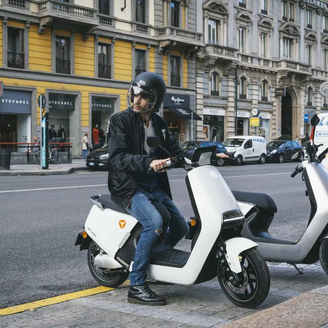 Oseba s čelado sedi na električnem skuterju Yadea G5, parkiranem na mestni ulici.