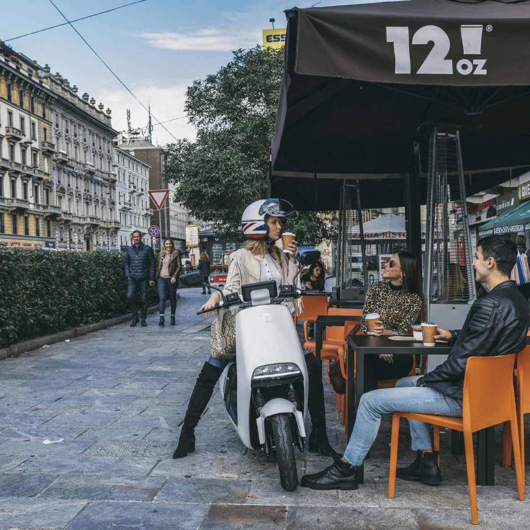 Ženska s čelado stoji ob električnem skuterju Yadea G5 blizu kavarne.