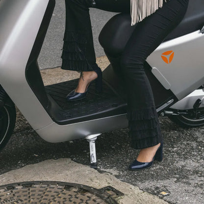 Oseba v elegantnih hlačah z resami in petah sedi na električnem skuterju Yadea G5.