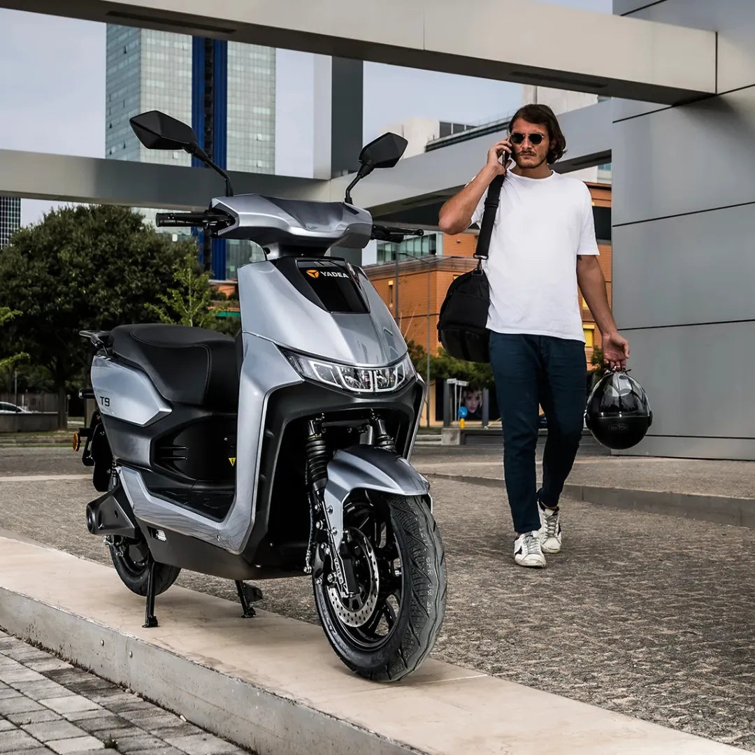 Moški hodi s čelado ob električnem skuterju Yadea T9l v urbanem okolju.
