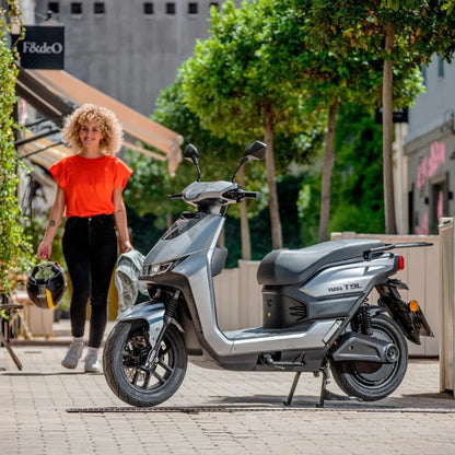 Ženska hodi proti električnemu skuterju Yadea T9l, parkiranem na sončni ulici.