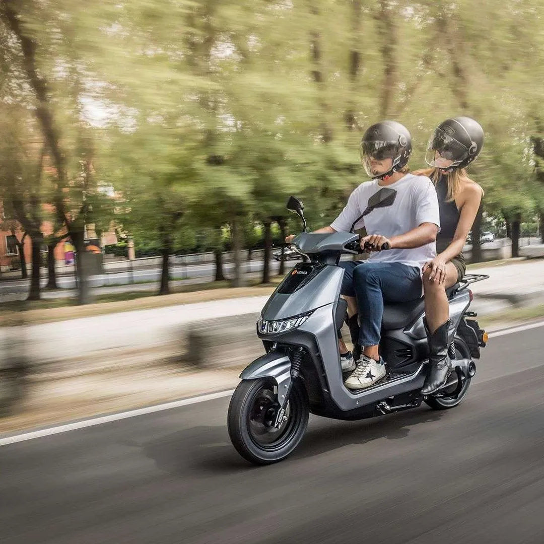 Moški in ženska se vozita z električnim skuterjem Yadea T9l po ulici z drevesi.