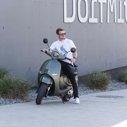 Moški sedi na električnem skuterju Efo Et5000 blizu sive stene, na kateri piše Dortmund.