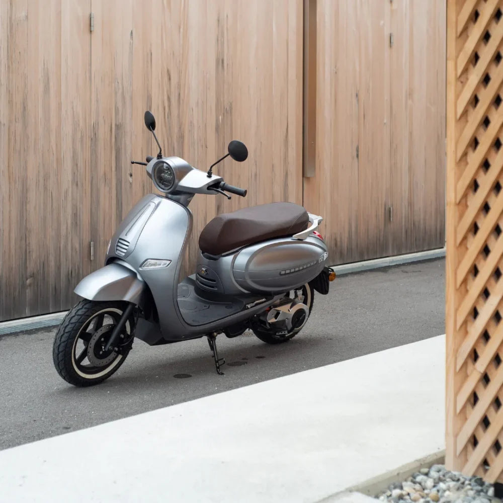 Električni skuter Efo Et3000 parkiran ob leseni steni, odlikuje ga eleganten srebrn dizajn.