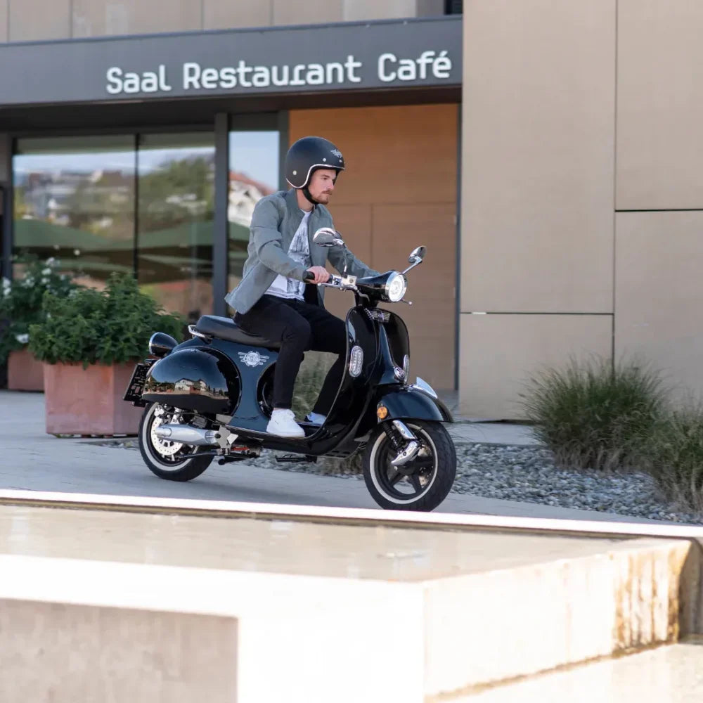 Moški se vozi z električnim skuterjem Efo Ev4000 blizu restavracije z moderno arhitekturo.