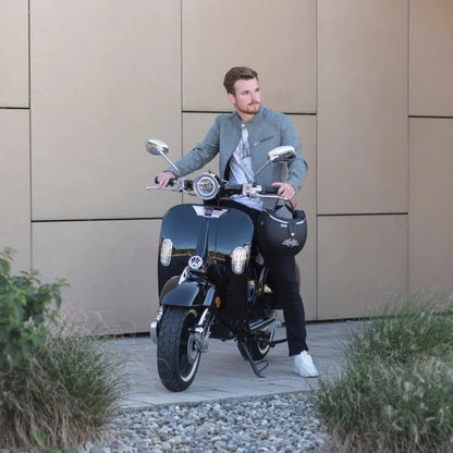 Moški v sivi jakni pozira na električnem skuterju Efo Ev4000 pred moderno kuliso.