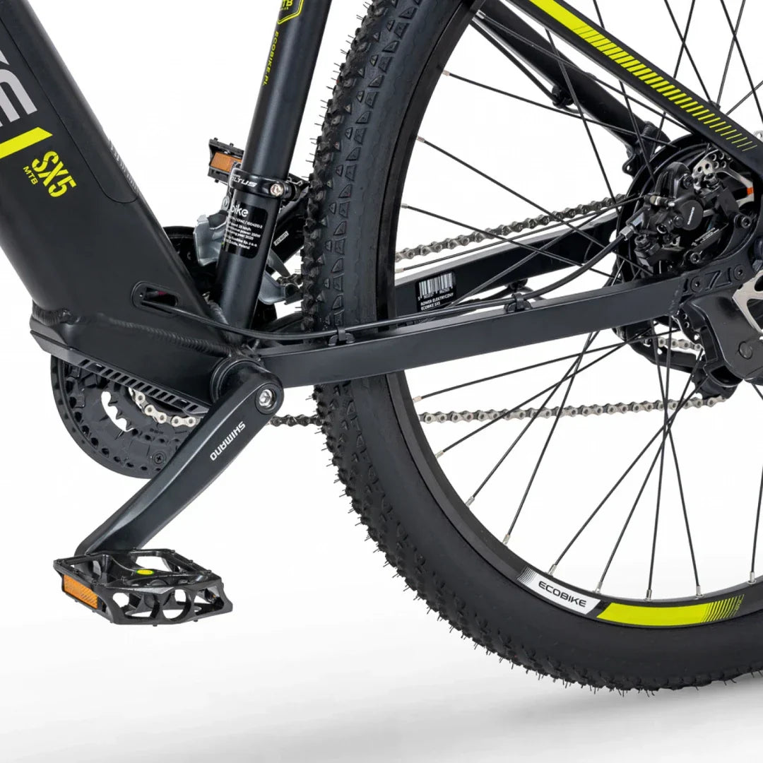 Na sliki je električno kolo znamke Ecobike, model SX5. Vidna je zadnja stran kolesa, kjer se nahajajo pedal, verižnik in amortizer. Kolo ima robustne pnevmatike, kar kaže na primernost za terensko vožnjo, ter sodoben dizajn z elementi v črni in rumeni barvi.